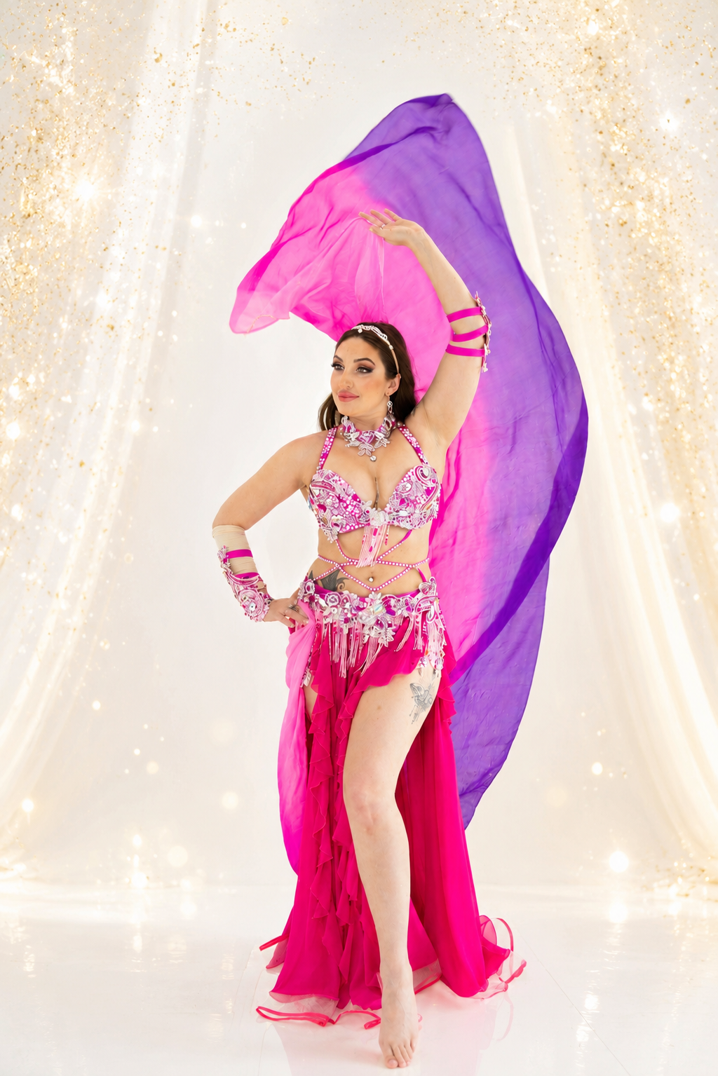 Dancer in a pink and purple costume with flowing fabric against a sparkling background